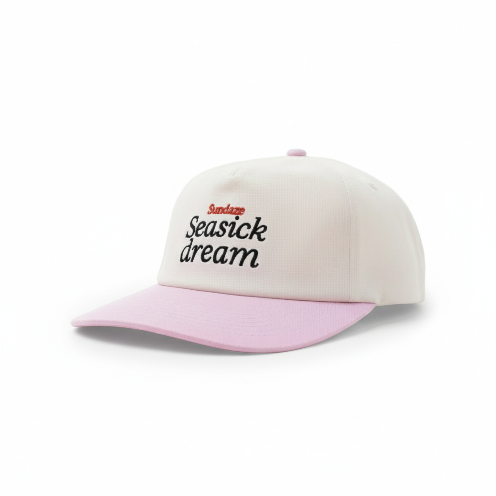 Pink and white cap with 'Seasick dream' text on a beach at sunset