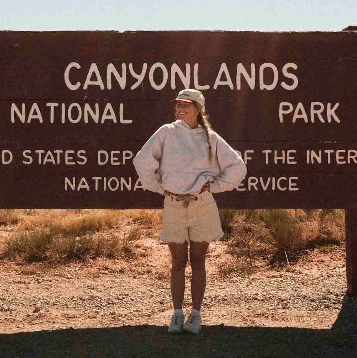 Person standing in front of Canyonlands National Park sign in a desert setting